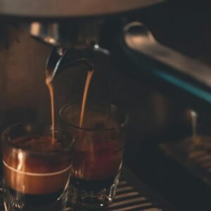 Close-up view of hot espresso pouring into two glasses, creating a rich coffee aroma indoors.